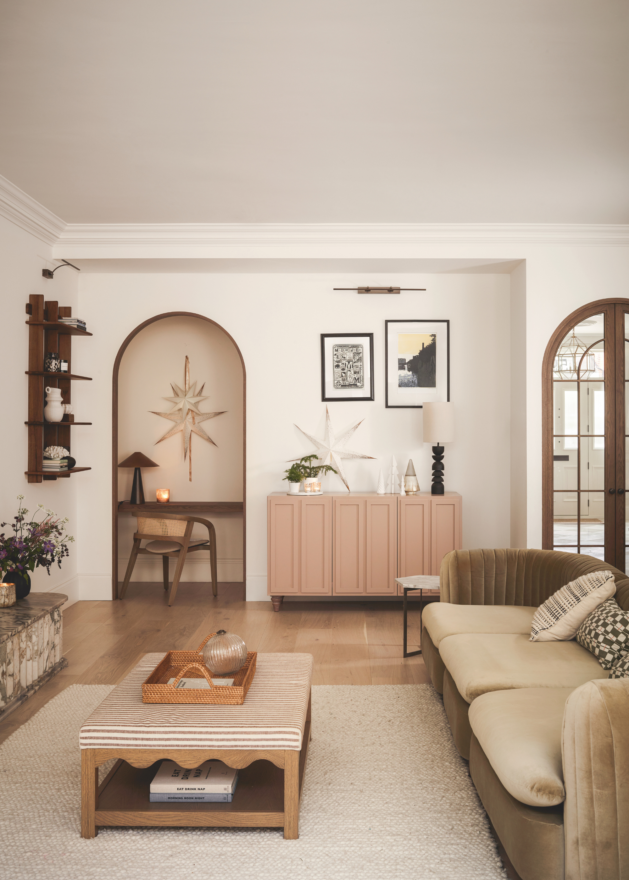 A neutral living room scheme with white paper star shades and white christmas tree decorations on the console table in among two arched doorways behind the sofa