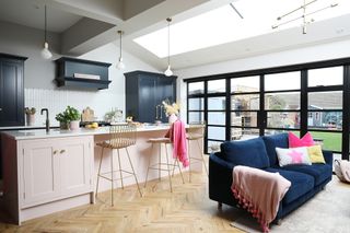 Kitchen-diner with herringbone floor, Crittall-style doors, dark blue Shaker-style kitchen with light pink island, and blue velvet sofa