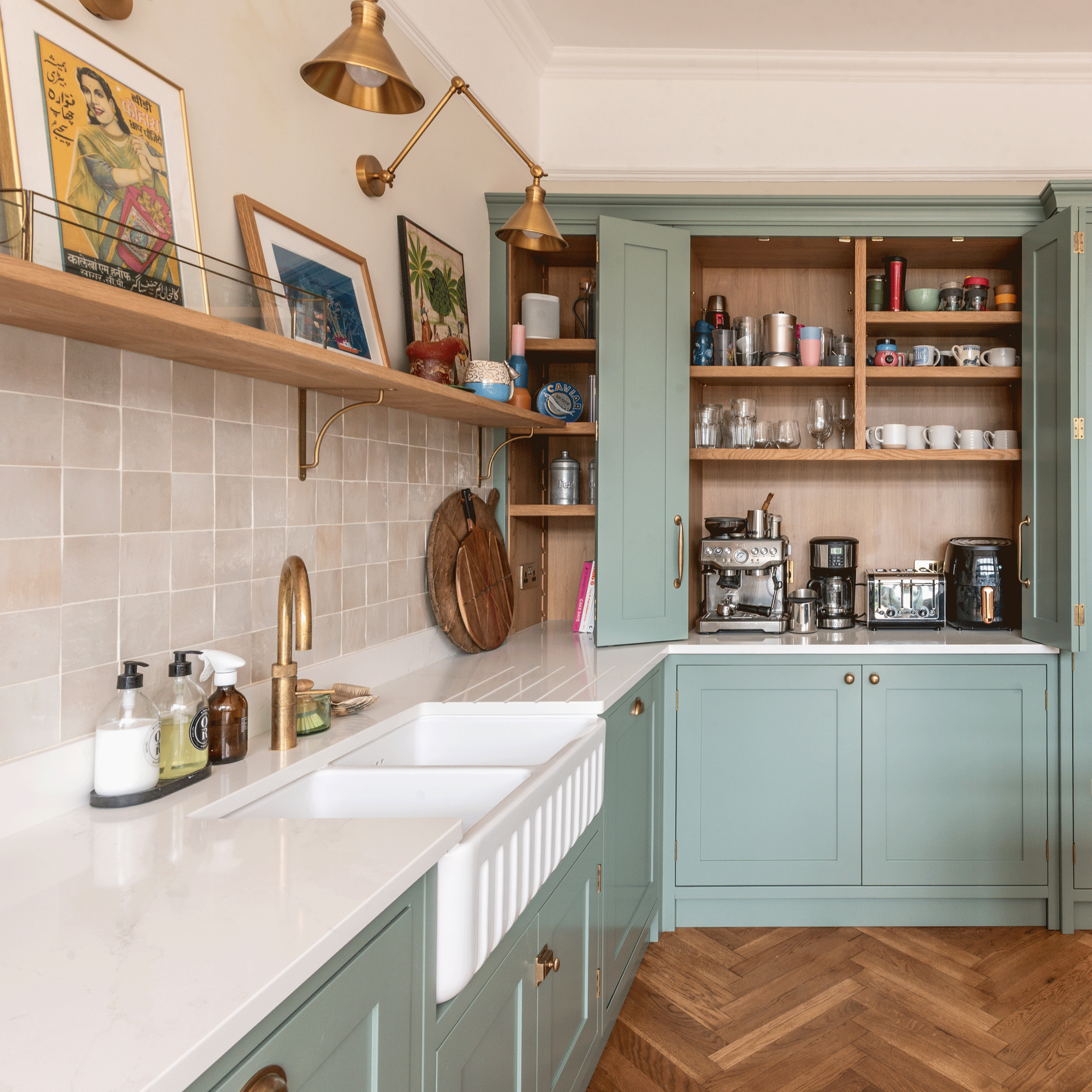 a kitchen with sage green cabinets and a fluted double Belfast sink with brass hot water tap, tiled splashback and open shelving and a cabinet with a coffee and tea station