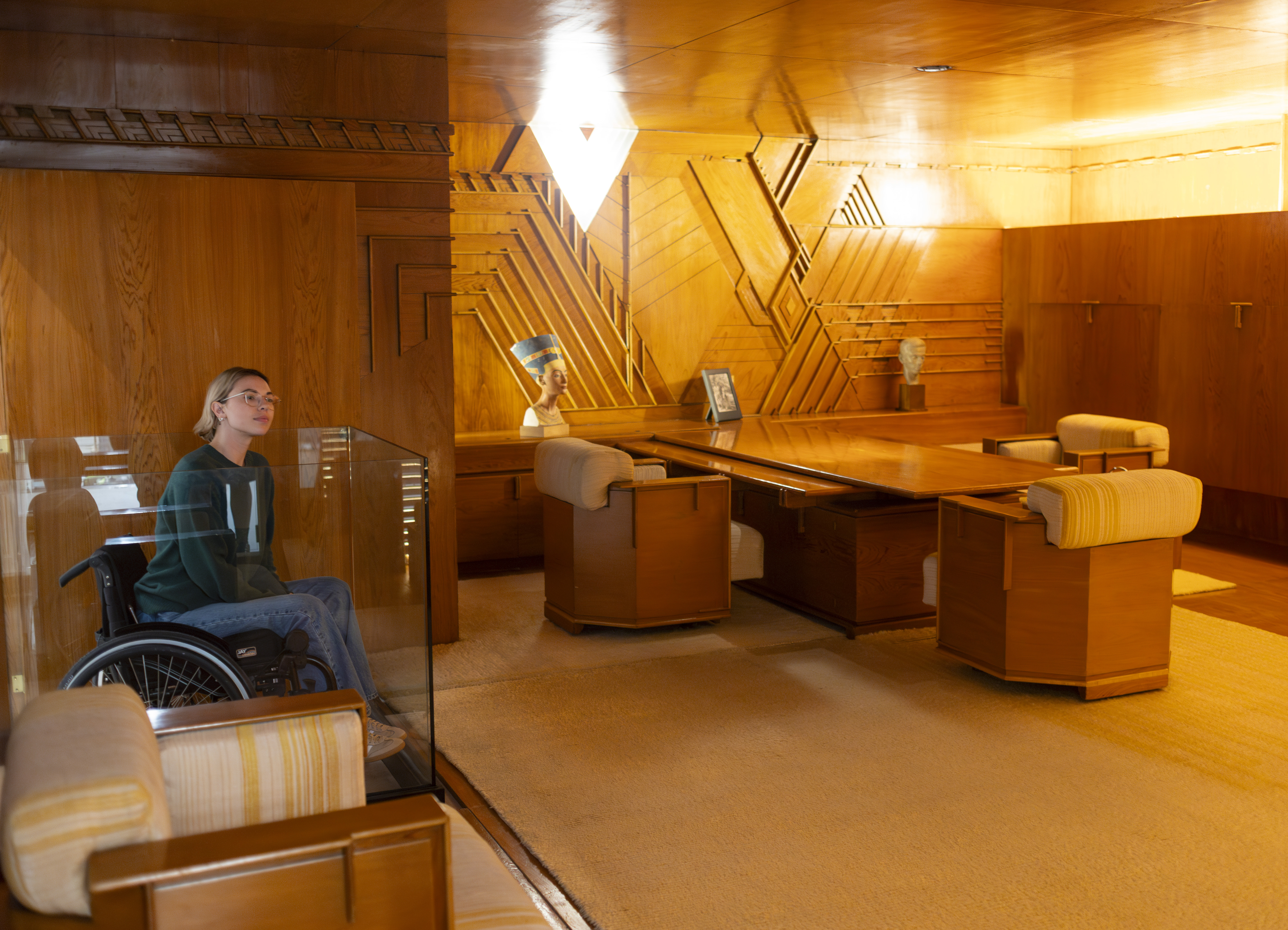A sumptuous, 1930s wood cabinetry sits in a warmly lit wing of a museum as a young woman observes it.
