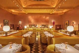 A rose and gold restaurant features eccentric, luxurious decor including quilted sofas, lamps, and shimmering cutlery.