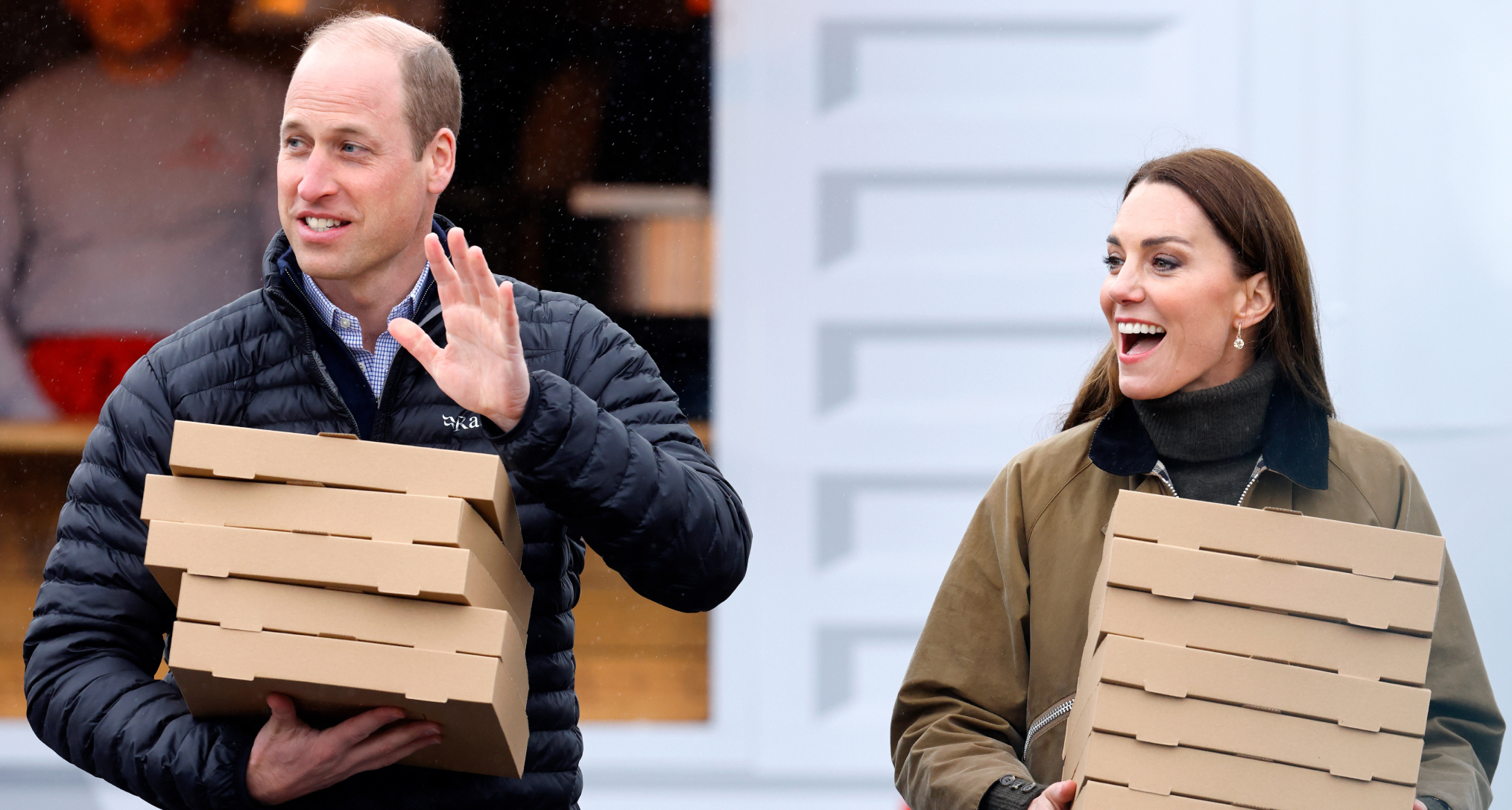 Prince William and Princess Kate smiling and carrying pizza boxes
