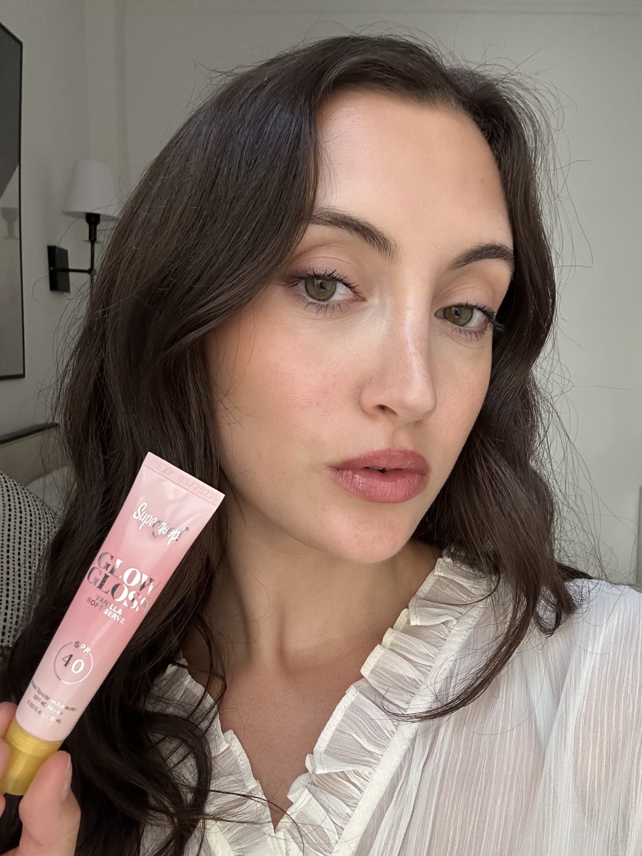 An image of Alyssa Brascia wearing and holding the Supergoop! Glow Gloss SPF 40 Lip Balm.