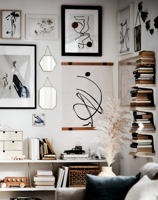 A white living room with books stacked on shelf and assortment of framed wall prints