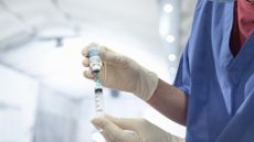a close up of a gloved nurse's hands as a prep a covid vaccine in a syringe