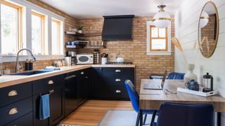 Navy blue kitchen with exposed brick wall with corner shelves to show a smart kitchen storage idea