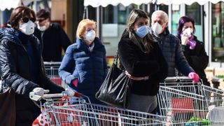 Residents wearing face masks wait outside a store in Codogno, southeast of Milan, Italy, on March 11, 2020, just a day after Italy imposed unprecedented national restrictions on its 60 million residents to help slow the spread of COVID-19.