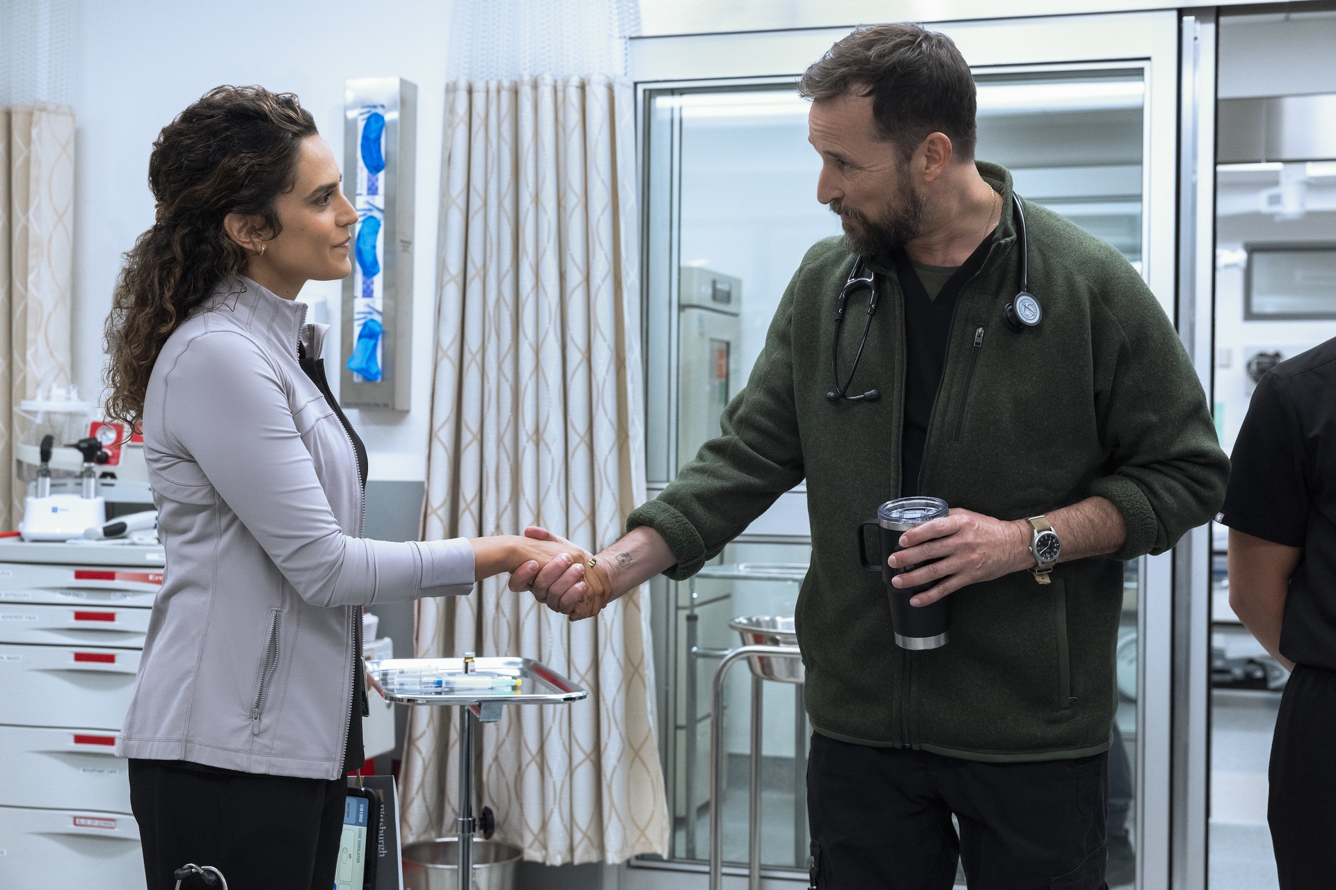 sepideh moafi as dr. al-hashimi and noah wyle as dr. robby shaking hands at the hospital and smiling at each other in a still from the pitt season 2