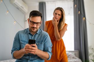 A man on his phone with a woman frowning over his shoulder