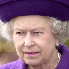 Queen Elizabeth wearing a purple hat and coat and scowling