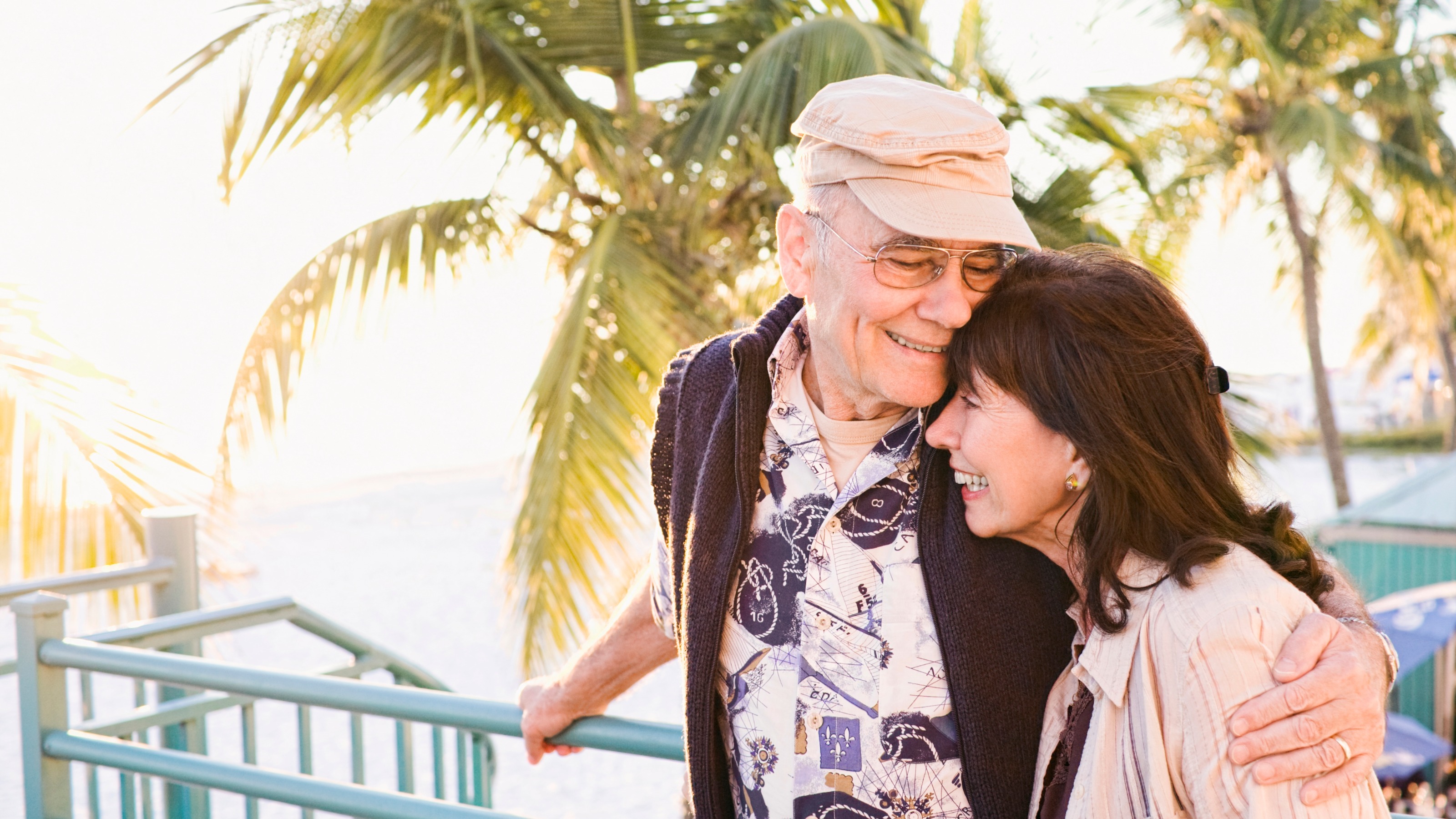 Older couple hugging, with a palm tree and the ocean in the background