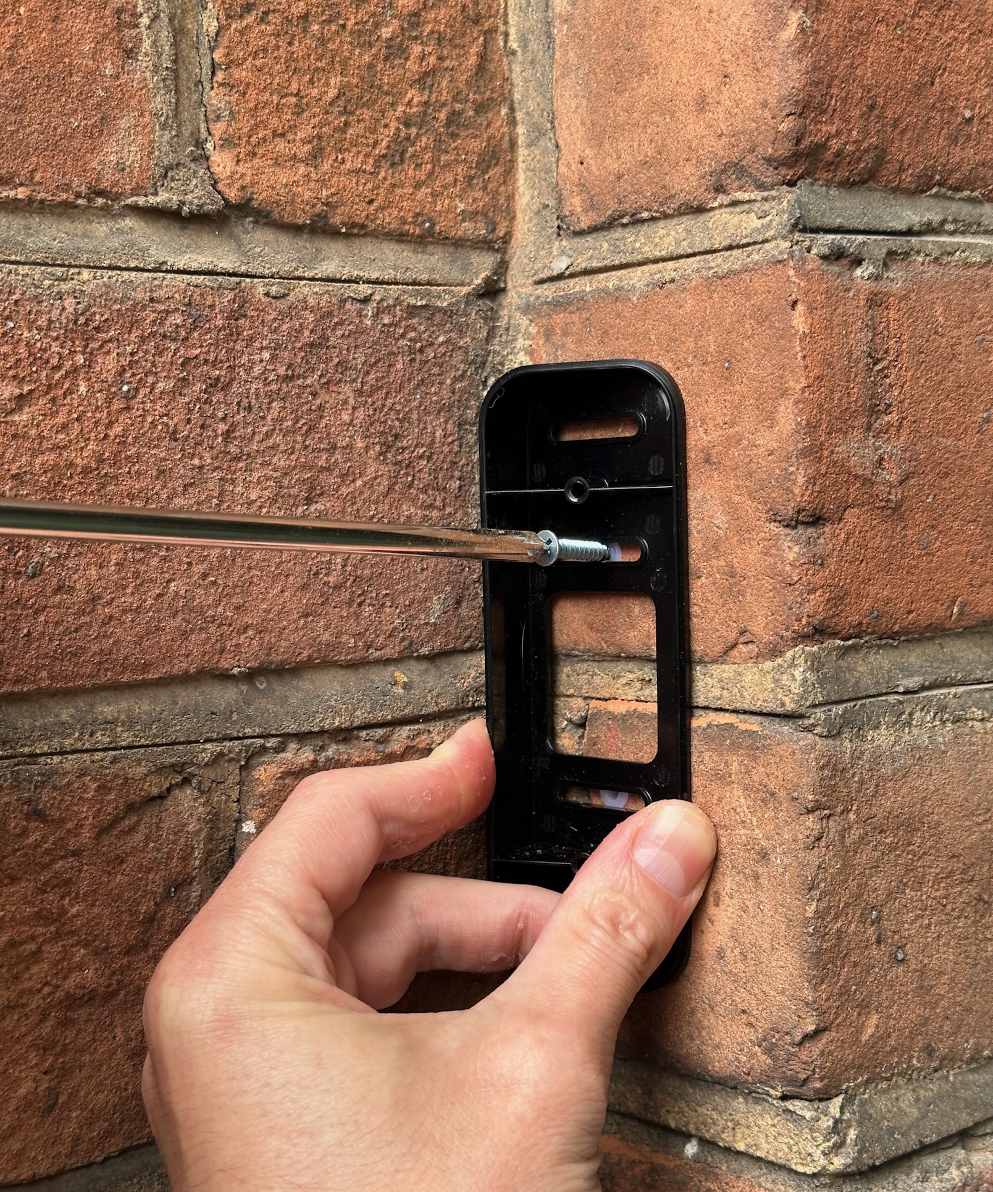 Screwing a Blink Video Doorbell mount into brick wall