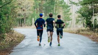 Three men running through a wood on a road