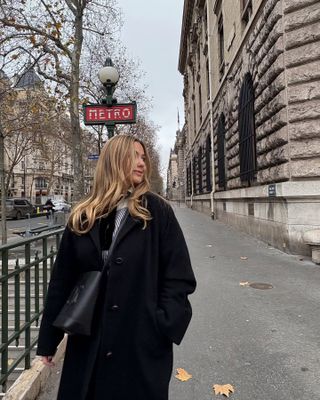 olivia wears long black coat with a handbag in paris