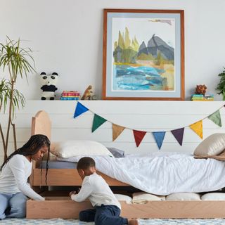 Two children in front of a Kids Trundle Bed Frame in a bedroom with flags and artwork on the walls.