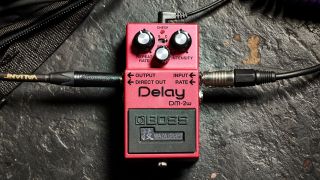 A Boss DM-2w delay pedal on the floor with guitar cables plugged into it