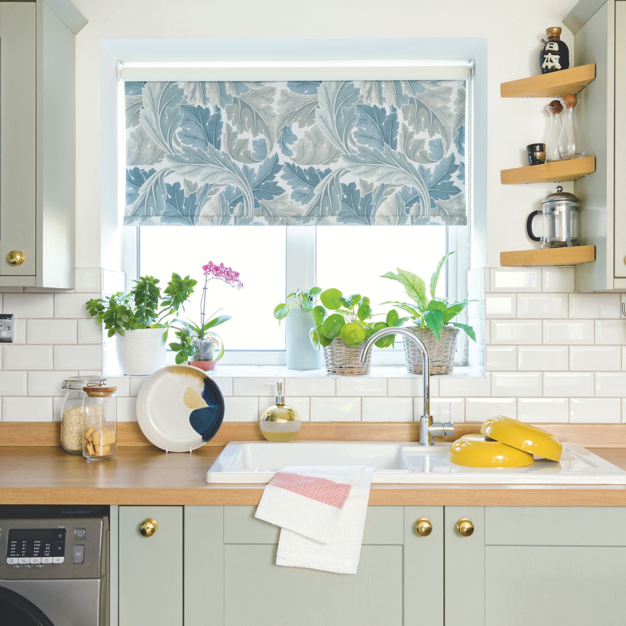 White painted kitchen with white metro tiles on the wall and a wooden worktop. The cabinets underneath are a light sage green