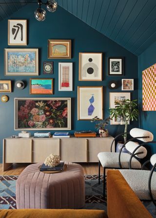 Living room with dark blue painted walls and sloped ceiling, gallery wall of art, and pink pouff
