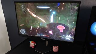 AOC AGON Pro AG246FK gaming monitor with Halo Infinite gameplay on screen with player and team under fire from energy weapons