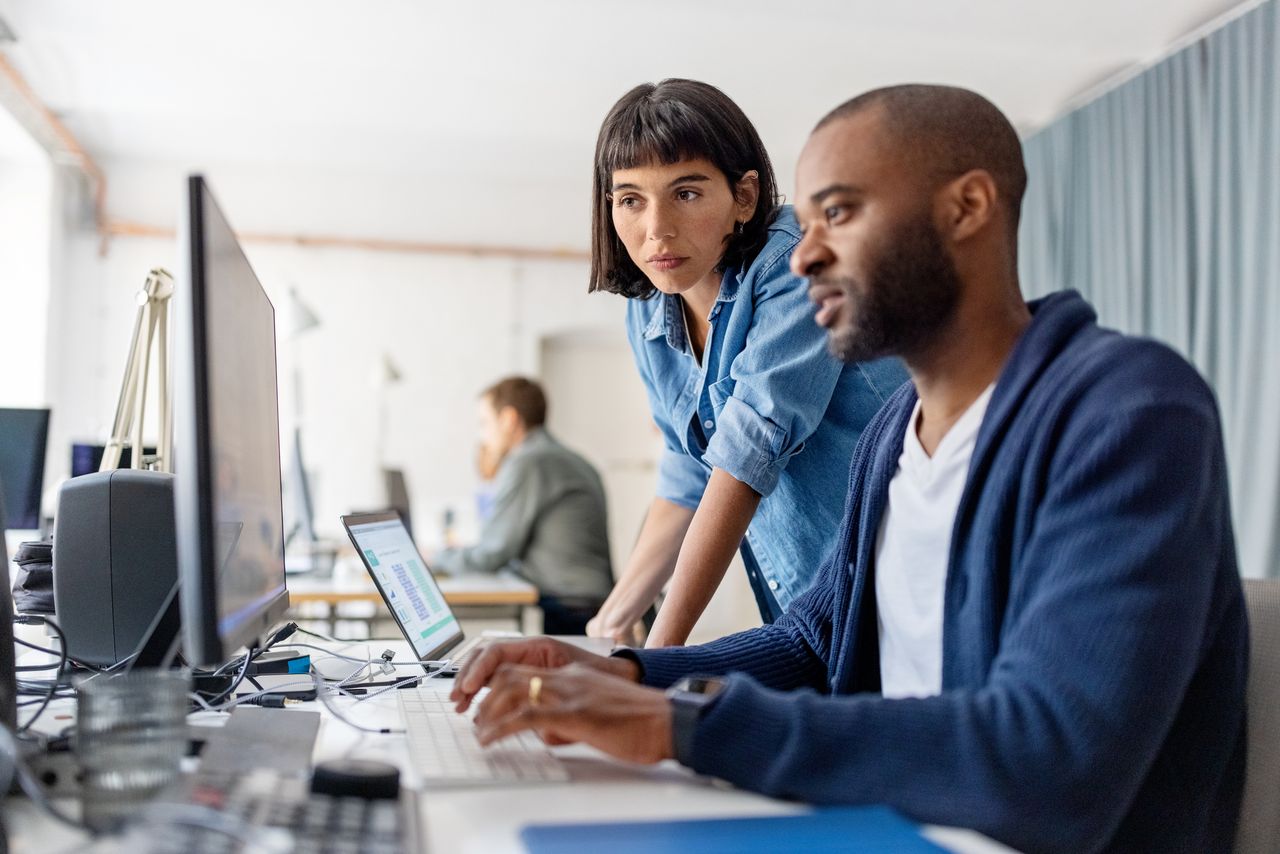 Two businesspeople looking at desktop computer monitor and discussing work at desk