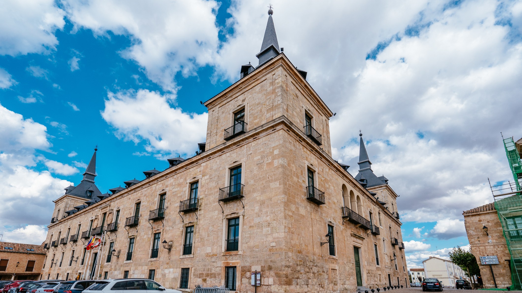 a light stone building with many windows and cars parked out front.