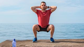 Man doing prisoner squat exercise near the water