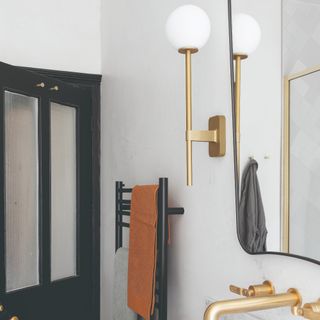 A bathroom with a brass wall sconce next to a mirror