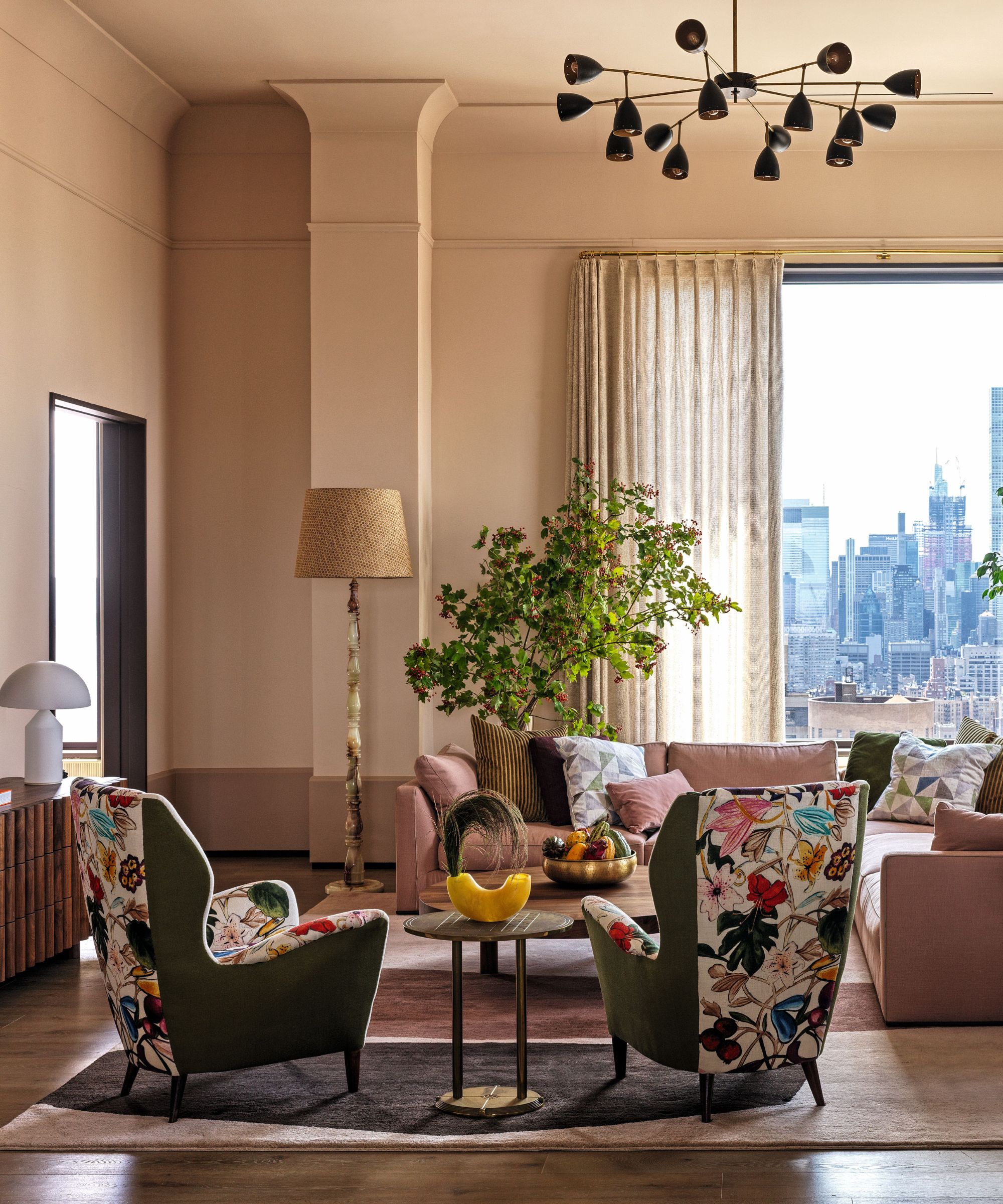Pale pink living room with pink corner sofa and two vintage chairs that have been re-upholstered in a colorful botanical print