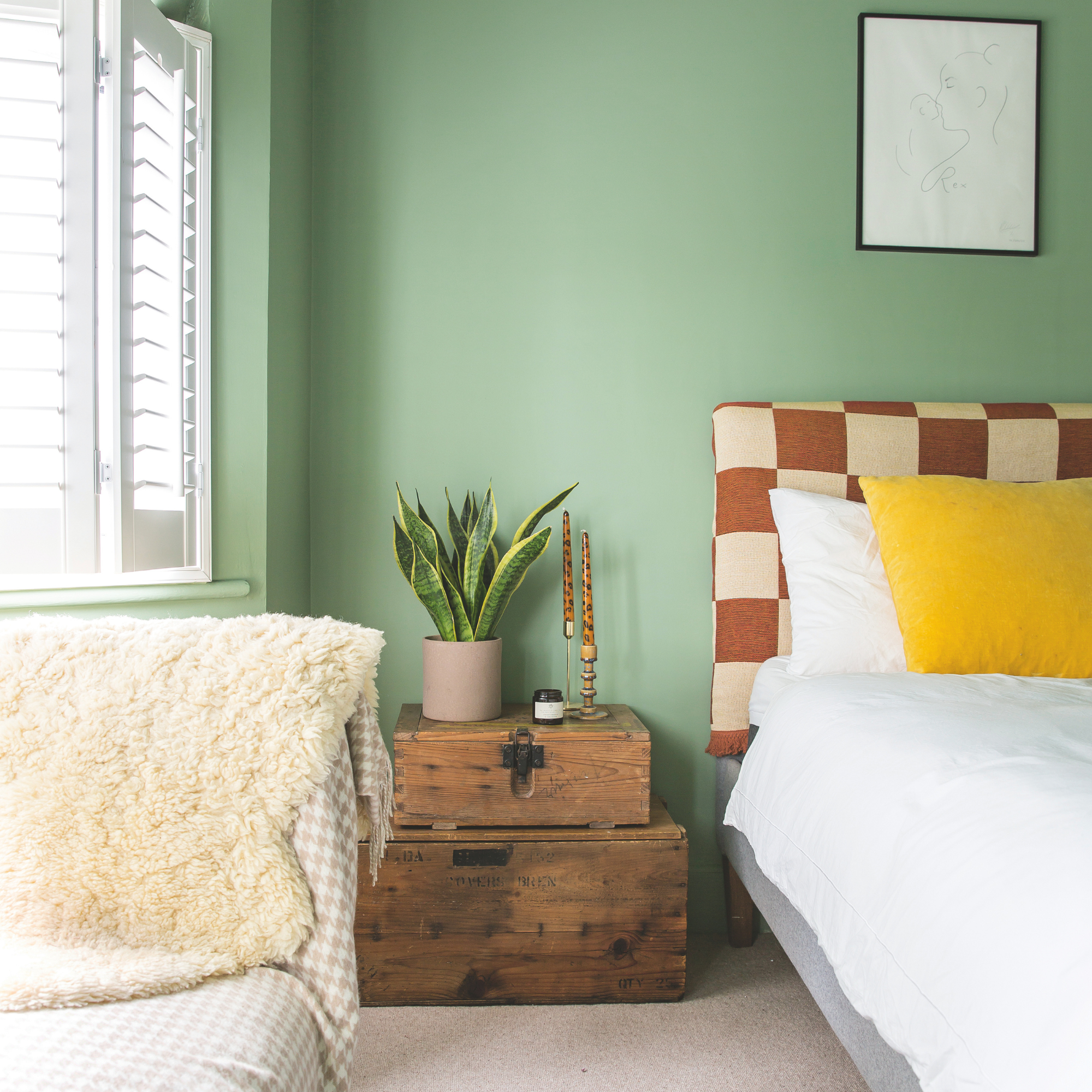 Sage green bedding, wood bedside table and bed with brown checkered headboard and white bedding.