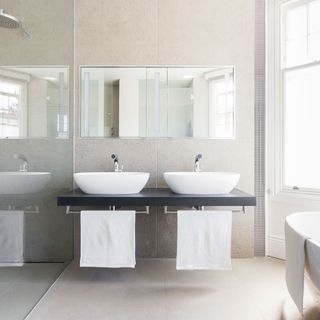 Wall-tiled bathroom with a mirror above white bathroom sinks next to a shower