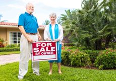 two older people next to house for sale sign