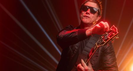 Paul Banks of Interpol adjusts the tuning on his Les Paul Custom, and wears a dark pair of sunglasses.