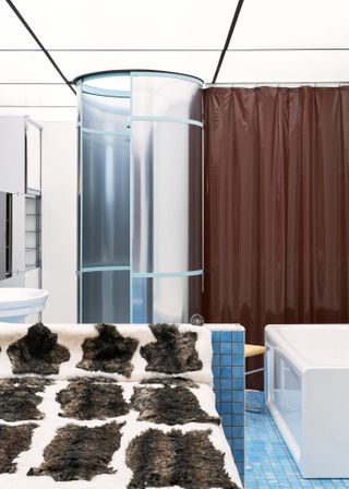 A bathroom tiled with small, sky blue tiles, a white tub, and bathroom sink, and a brown shower curtain.