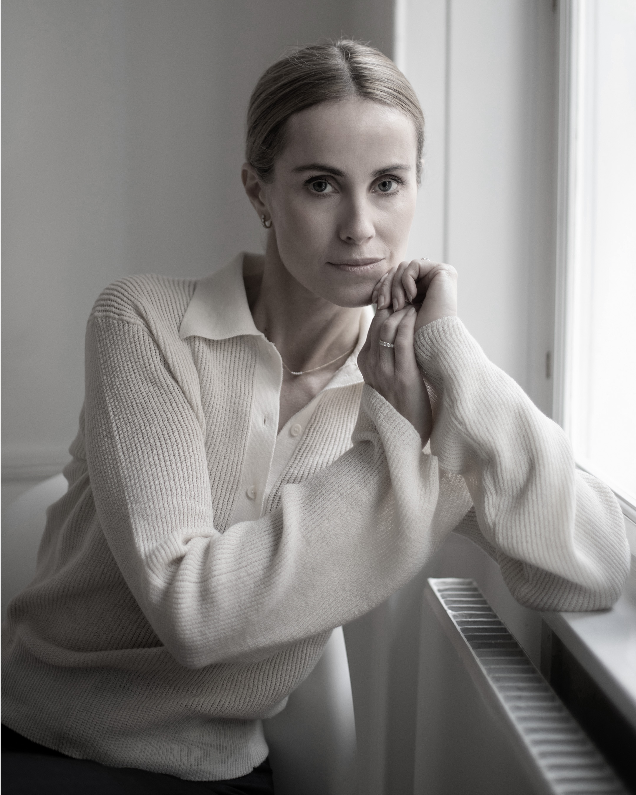 Cecilie Thorsmark seated by a window, resting her chin on her hands, wearing a light sweater.
