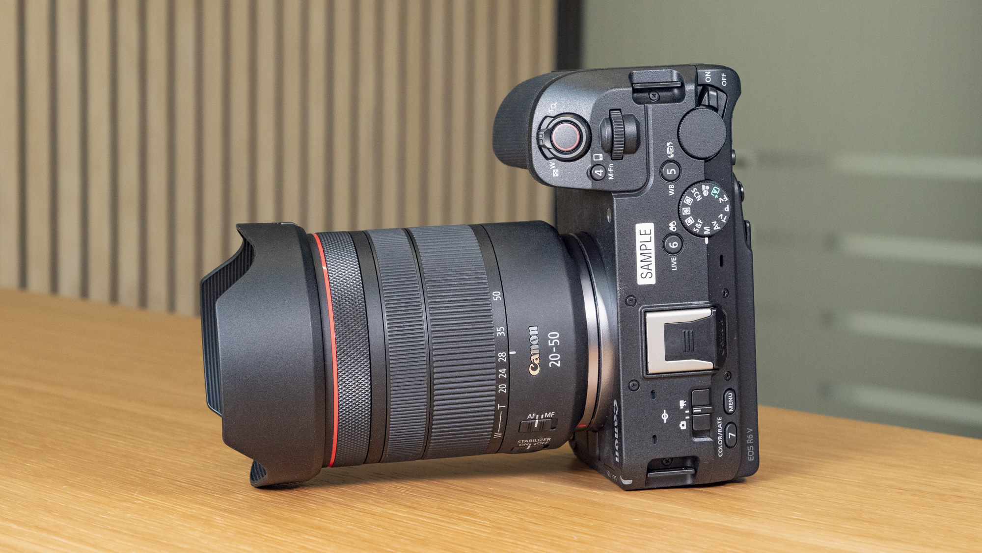 The Canon EOS R6 V mirrorless camera on a wooden table with a pine-slatted backdrop, no lens attached