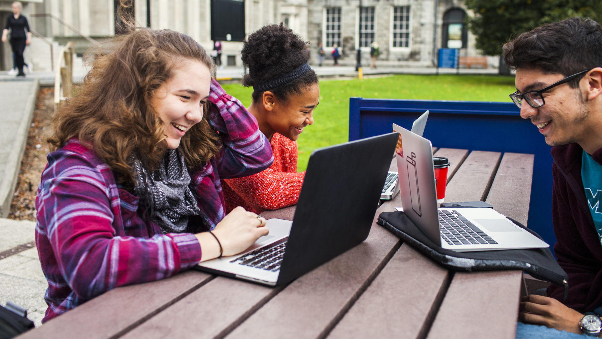 Smiling university students with laptops on table at campus