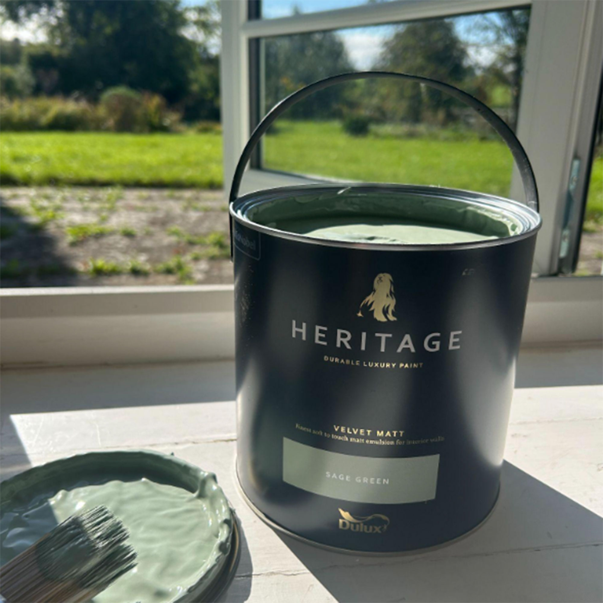 Open can of Dulux Heritage sage green paint sitting on indoor windowsill