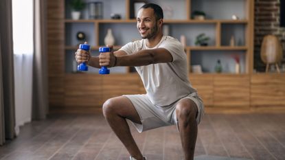 Man squats down at home holding dumbbells out in front of him