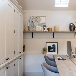 A home office with built-in storage cabinets, a double desk with two chairs and a floating shelf displaying decor