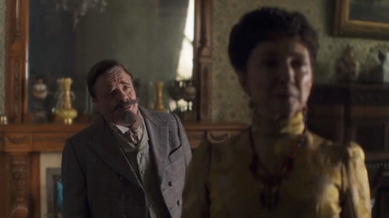 Mrs. Astor in the foreground looking angry with Ward McAllister in the background looking upset in The Gilded Age
