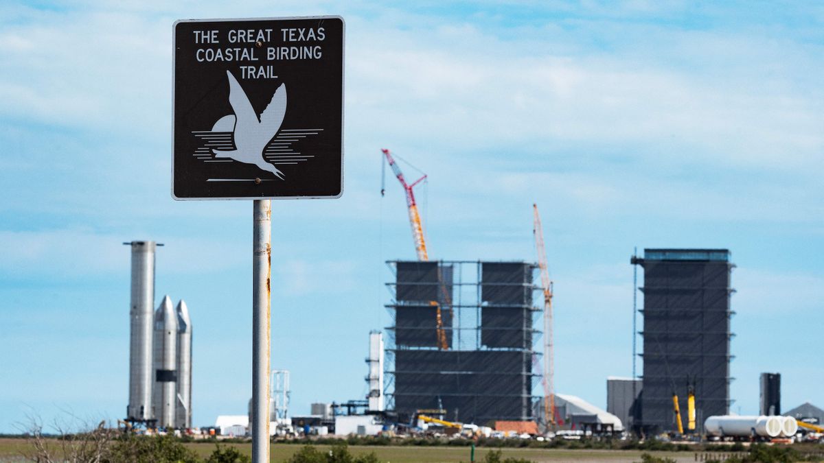 a sign that says &#039;the great texas coastal birding trail&#039; stands in front of spacex hardware and pieces of spacex starship, all far in the background