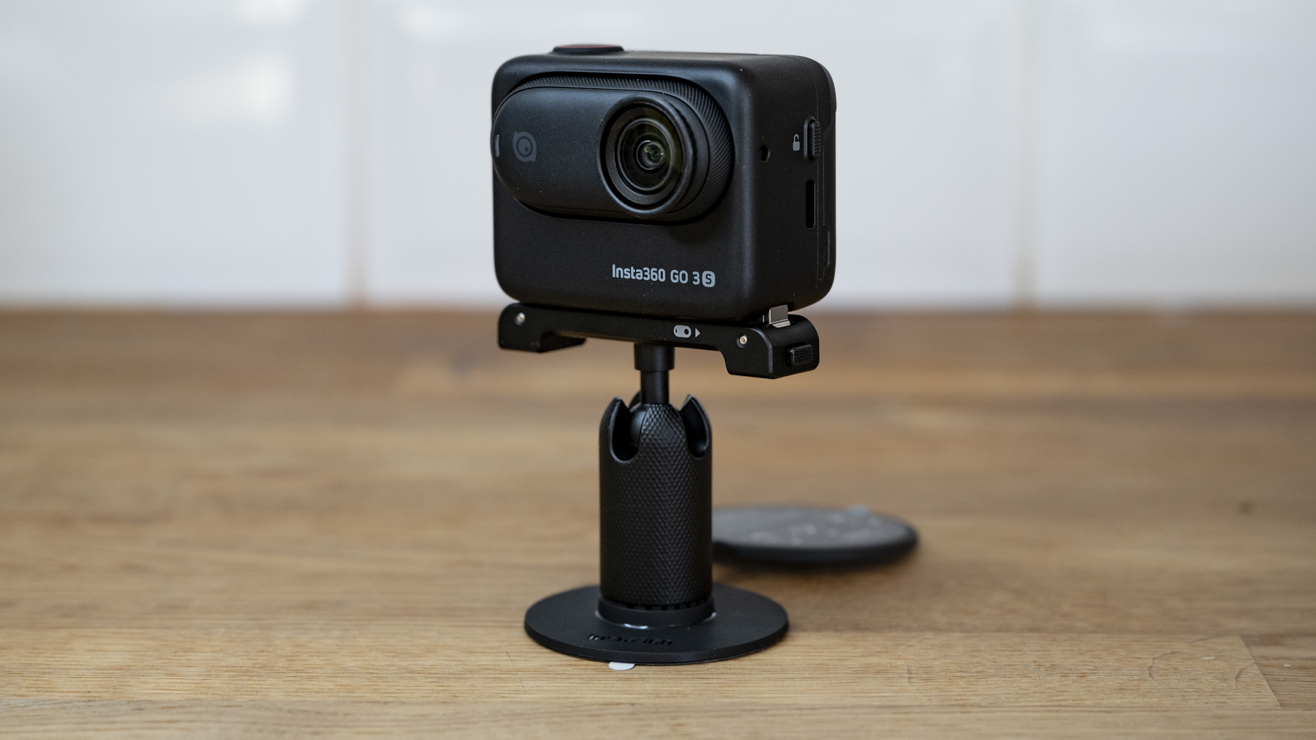 Insta360 Go 3S camera in its housing and attached to an accessory on a wooden surface