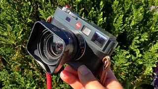 The Leica 28mm Elmarit-M f/2.8 V3 attached to a Leica M9 against a green bush