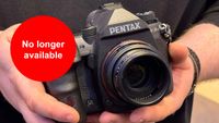 Hands holding a Pentax K-3 Mark III Monochrome camera with a lens. A red circle with white text states "No longer available"