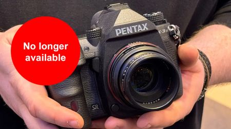 Hands holding a Pentax K-3 Mark III Monochrome camera with a lens. A red circle with white text states "No longer available"