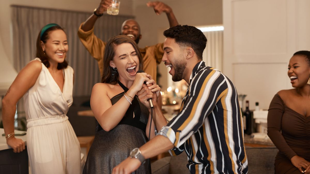 A group of people doing karaoke. Two people at the front are singing together, with their friends cheering and singing along in the background.