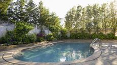 A backyard pool surrounded by flower beds and trees