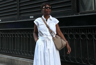 woman wearing loewe bag, white sundress, and sunglasses against black street background