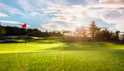 A golf hole on the green with the sun setting behind it