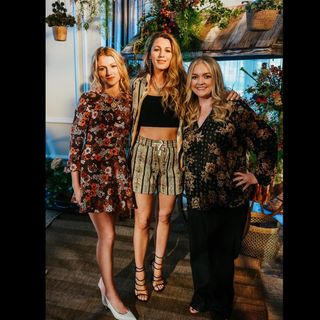 Blake Lively poses with women working on the It Ends With Us film adaptation while wearing a Bode shirt borrowed from Ryan Reynolds and a pair of Versace heels
